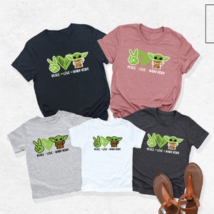 K&ouml;nnte beinhalten: Satz von f&uuml;nf T-Shirts mit einem gr&uuml;nen Comic-Charakter mit dem Text "Peace Love Baby Yoda". Die Shirts sind in verschiedenen Farben, darunter Schwarz, Grau, Wei&szlig; und Rosa.
