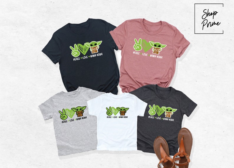 K&ouml;nnte beinhalten: Satz von f&uuml;nf T-Shirts mit einem gr&uuml;nen Comic-Charakter mit dem Text "Peace Love Baby Yoda". Die Shirts sind in verschiedenen Farben, darunter Schwarz, Grau, Wei&szlig; und Rosa.