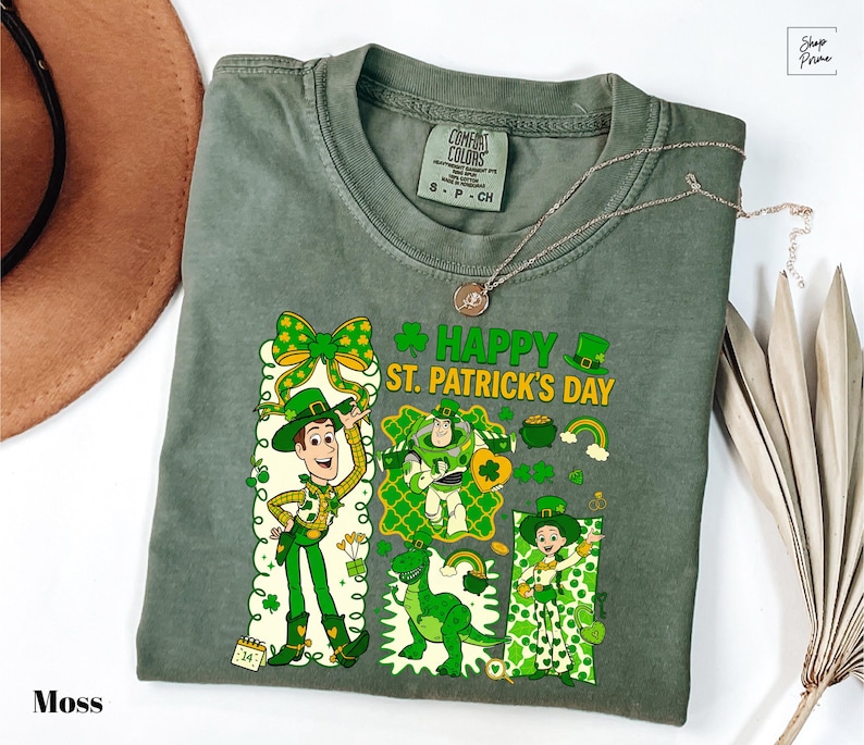 A green t-shirt with a cartoon character and text printed on it, along with a hat and some leaves, all placed on a white surface.
