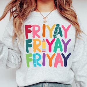 May include: A gray sweatshirt with the word "FRIYAY" repeated three times in colorful, stylized lettering. Each word is decorated with a different school supply: a ruler, a pencil, and a ruler.