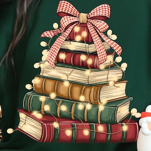 May include: A dark green sweatshirt featuring a stack of books arranged in a Christmas tree shape. The books are adorned with a red and white plaid bow and string lights. A festive holiday design.