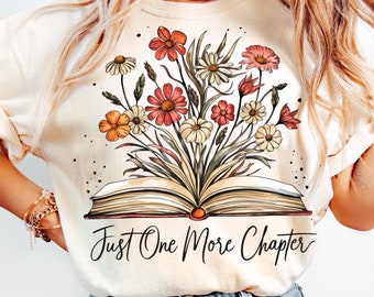 May include: A cream-colored t-shirt with a graphic of an open book with flowers growing out of it. The text "Just One More Chapter" is printed below the book.