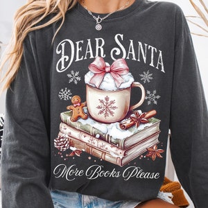 May include: Dark gray sweatshirt with the text "Dear Santa More Books Please." The graphic features a mug of hot chocolate with whipped cream and a pink bow, a gingerbread man, and books.
