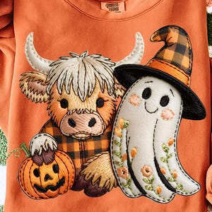 Könnte beinhalten: Oranges Sweatshirt mit gesticktem Halloween-Design. Es zeigt eine Hochlandkuh in einem karierten Hemd, einen Geist mit Hexenhut und einen Kürbis. Das Sweatshirt hat einen Rundhalsausschnitt und lange Ärmel.