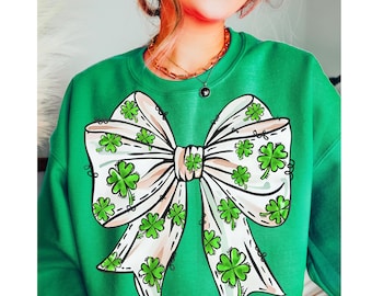 Peut inclure: Sweat-shirt vert avec un nœud blanc imprimé sur le devant. Le nœud est décoré de motifs de trèfles à quatre feuilles verts.