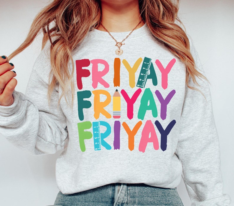 May include: A gray sweatshirt with the word "FRIYAY" repeated three times in colorful, stylized lettering. Each word is decorated with a different school supply: a ruler, a pencil, and a ruler.