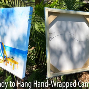 May include: A hand-painted canvas print of a beach scene with two blue and white striped beach chairs, a table with a drink, and a blue sky with white clouds. The canvas is wrapped around a wooden frame and is ready to hang.