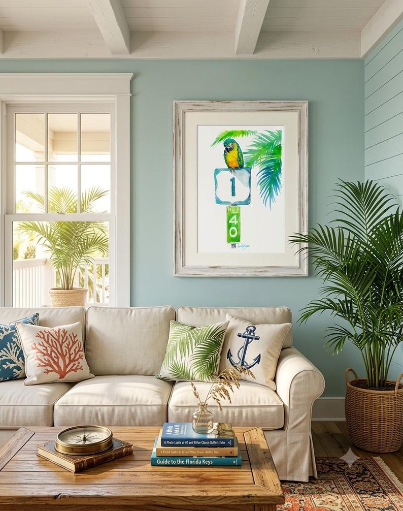Bright coastal living room decor mockup featuring a framed tropical watercolor print by David K Jones titled A Parrot Looks at 40. The artwork hangs blue wall, creating a beach house aesthetic.