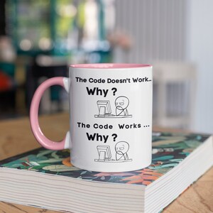 May include: White coffee mug with a pink rim and handle. The mug has a black design with the text "The Code Doesn't Work... Why?" and "The Code Works... Why?" with a stick figure illustration of a person at a computer for each text.