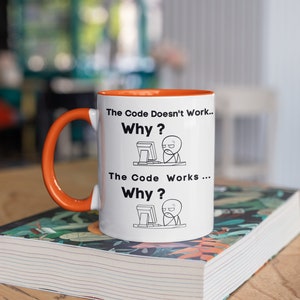 May include: White ceramic mug with an orange rim and handle. The mug features a black and white illustration of a person at a computer with the text "The Code Doesn't Work... Why?" and "The Code Works... Why?"