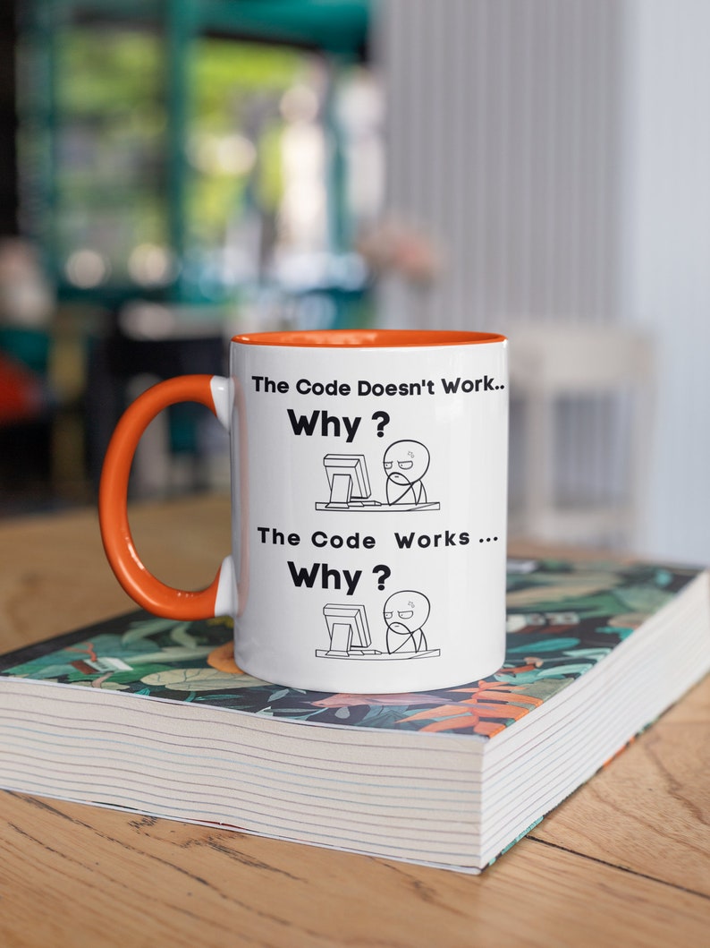 May include: White ceramic mug with an orange rim and handle. The mug features a black and white illustration of a person at a computer with the text "The Code Doesn't Work... Why?" and "The Code Works... Why?"