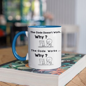 May include: White ceramic mug with a blue rim and handle. The mug features a black and white illustration of a person at a computer with the text "The Code Doesn't Work... Why?" and "The Code Works... Why?"