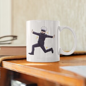 May include: White ceramic mug with a cartoon illustration of a character with white hair and a black eye mask running with their arms outstretched. The character is wearing a black jacket and black pants. The background is white.