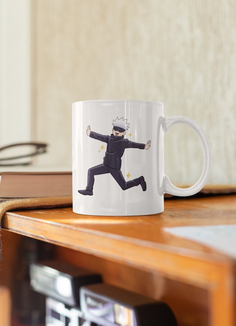 May include: White ceramic mug with a cartoon illustration of a character with white hair and a black eye mask running with their arms outstretched. The character is wearing a black jacket and black pants. The background is white.