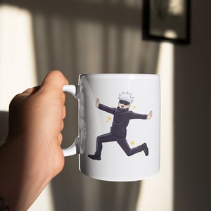 May include: White ceramic mug with a cartoon illustration of a character with white hair and a black mask, wearing a black suit and running with arms outstretched. The character is surrounded by small yellow stars.