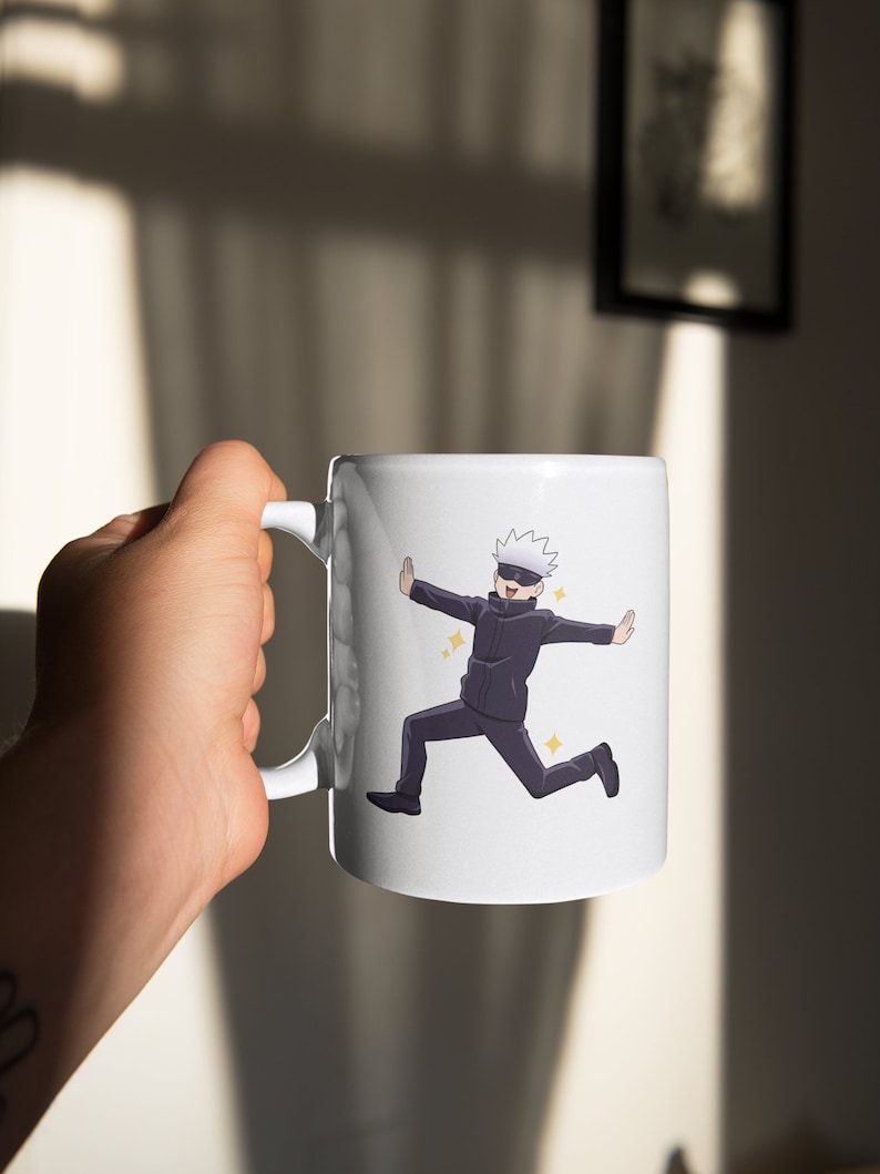 May include: White ceramic mug with a cartoon illustration of a character with white hair and a black mask, wearing a black suit and running with arms outstretched. The character is surrounded by small yellow stars.