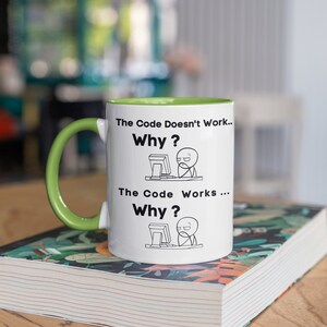 May include: White ceramic mug with a green rim and handle. The mug features a black and white illustration of a person at a computer with the text "The Code Doesn't Work... Why?" and "The Code Works... Why?"