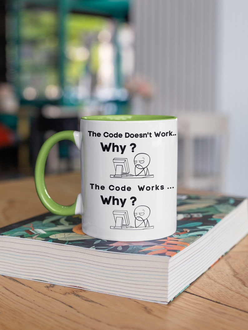 May include: White ceramic mug with a green rim and handle. The mug features a black and white illustration of a person at a computer with the text "The Code Doesn't Work... Why?" and "The Code Works... Why?"