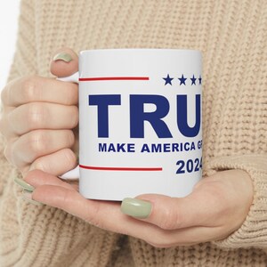 May include: White ceramic mug with a blue and red design. The mug features the text "TRUMP MAKE AMERICA GREAT AGAIN 2024" with five stars above the word "TRUMP".