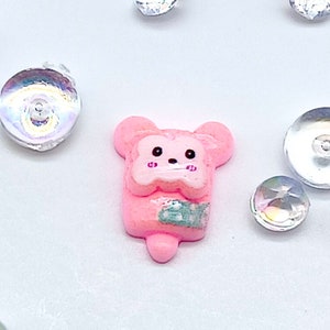 Puede incluir: Encanto de resina en forma de oso rosa con un diseño azul claro y blanco. El encanto está rodeado de lentejuelas iridiscentes.