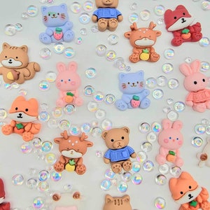 Puede incluir: Surtido de encantos de arcilla polimérica hechos a mano de colores, con varios diseños de animales, incluyendo gatos, osos, zorros, ciervos, conejos y un cordero. Los encantos están decorados con detalles como suéteres, zanahorias y fresas.