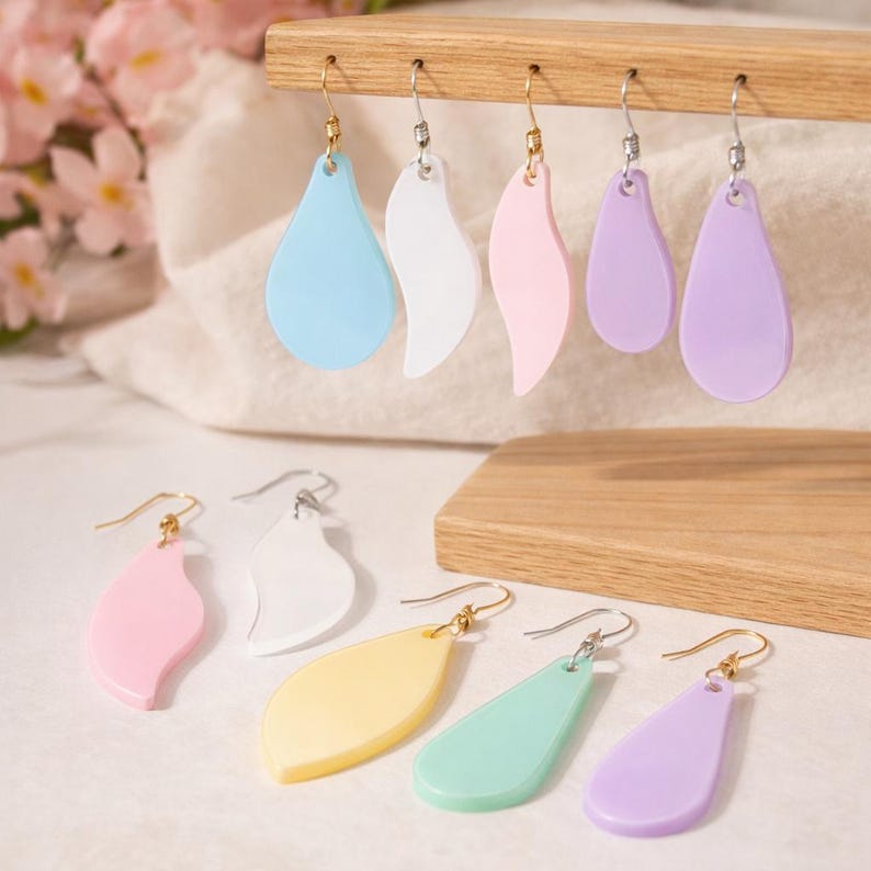 May include: A selection of pastel-coloured earrings in teardrop and leaf shapes. The earrings are displayed on a wooden stand. Colours include blue, white, pink, yellow, green, and purple. The earrings have gold and silver hooks.