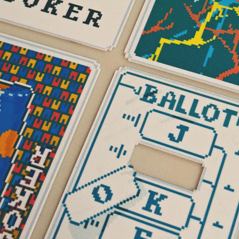 May include: Close-up of playing cards with pixelated designs. The cards feature blue, yellow, red, and white graphics. One card reads "JOKER" in black pixelated letters. Another card has the word "BALLOT" in blue pixelated letters.
