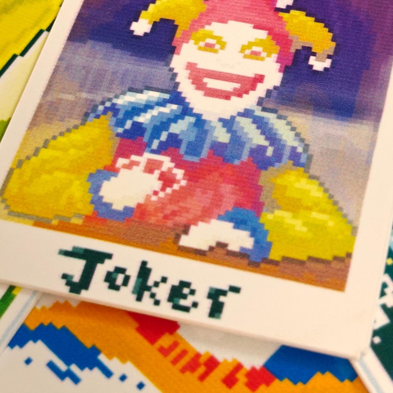 May include: A playing card featuring a pixelated jester with a pink face, yellow hat, and blue collar. The word "Joker" is printed in green block letters at the bottom of the card. Other cards are visible in the background.