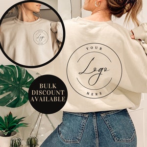 May include: A beige sweatshirt with a round logo that says "YOUR LOGO HERE" on the back. The sweatshirt is being modeled by a person wearing blue jeans.