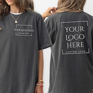 May include: Pepper-colored t-shirts with the text "YOUR LOGO HERE" in a white rectangular frame on the front and back. The shirts are short-sleeved and have a relaxed fit. The front of the shirt also has the text "CUSTOM LOGO".
