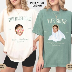 May include: Two t-shirts with different designs for a bachelorette party. The ivory shirt has a light green print that says "The Bach Club" with a woman's face wearing sunglasses. The light green shirt has an ivory print that says "The Bride" with a woman's face wearing a veil.