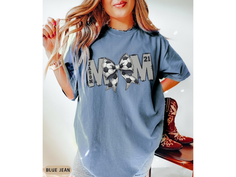 May include: A blue jean t-shirt with the word "MOM" in white letters with a soccer ball bow in the middle. The text "JASON 21" is on the shirt.