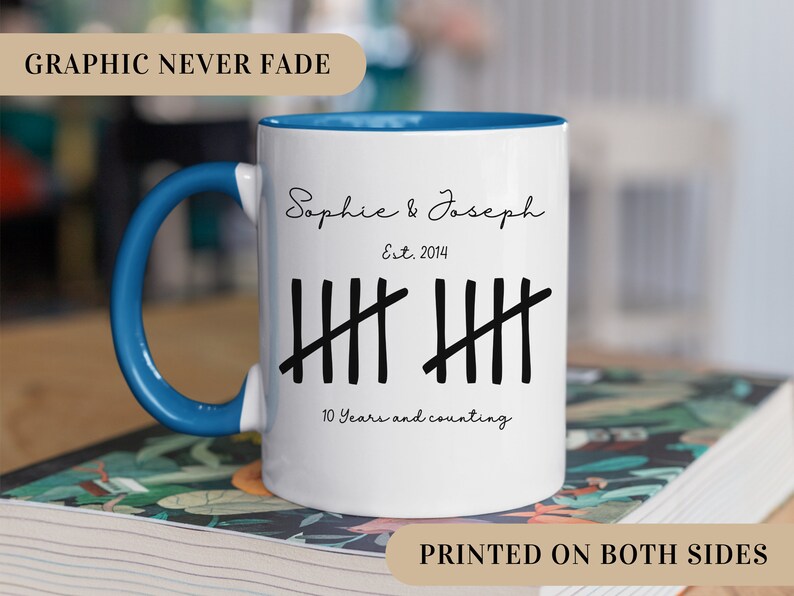 May include: White ceramic mug with a blue handle. The mug has a black graphic that says "Sophie & Joseph Est. 2014" and has ten tally marks with the text "10 Years and counting".
