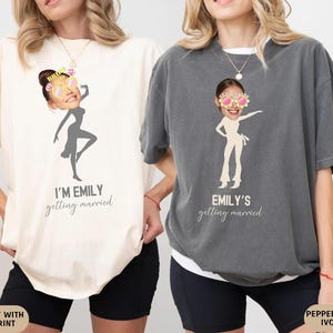 May include: Two ivory and pepper t-shirts with a graphic of a woman dancing and the text "I'm Emily getting married" and "Emily's getting married".