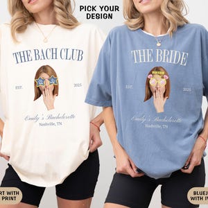 May include: Two white t-shirts with blue text and graphics. The text on the left shirt reads "The Bach Club Est. 2025" and the text on the right shirt reads "The Bride Est. 2025". Both shirts feature a cartoon image of a woman wearing sunglasses and covering her mouth with her hand.