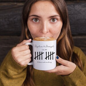 May include: White ceramic mug with black text and markings. The text reads "Sophie & Joseph Est. 2014" and "10 Years and counting".