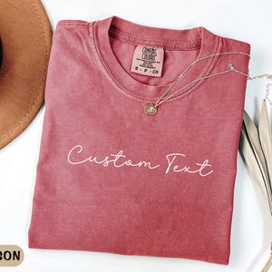 May include: Crimson red t-shirt with a white "Custom Text" design. The shirt is made of a soft, comfortable fabric and has a relaxed fit.
