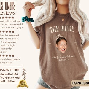 May include: A brown t-shirt with the text "THE BRIDE" in white, a crown, and a photo of a woman's face. The text "EST. 2015" is below the crown. The text "Emily's Bachelorette Nashville, TN" is below the photo.