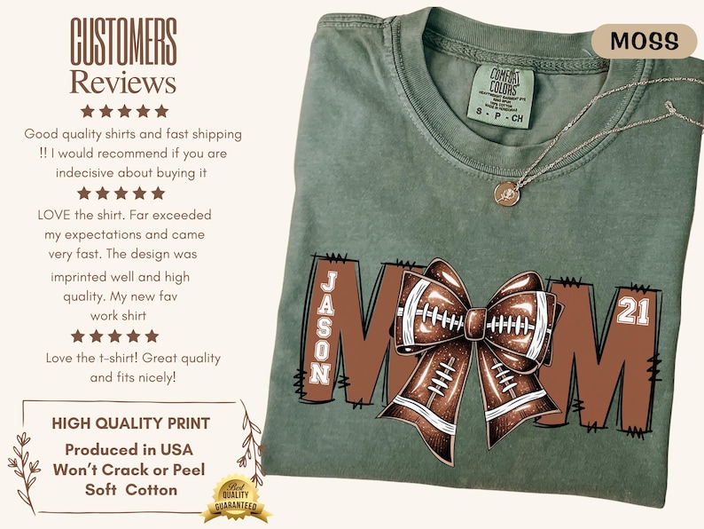 May include: Moss green t-shirt with a football-themed design. The word "MOM" is displayed in brown block letters, with a football bow in the center. The name "JASON" and the number "21" are also visible. A silver necklace is draped on the shirt.