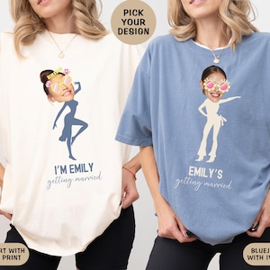 May include: Two t-shirts with a bride-to-be theme. The ivory shirt has blue text that says "I'm Emily getting married". The blue jean shirt has ivory text that says "Emily's getting married". Both shirts feature a silhouette of a woman with a bride's veil and sunglasses.