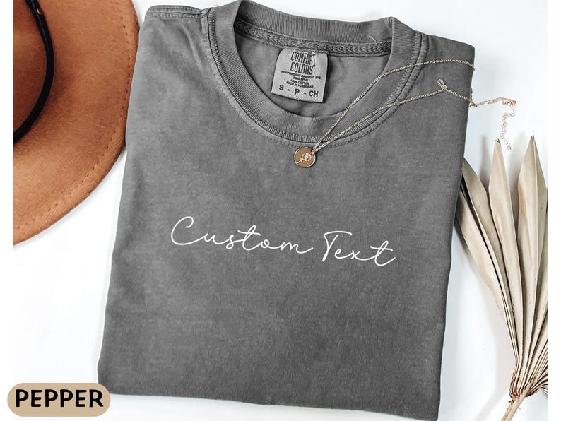 May include: A gray,  comfy-looking t-shirt with the text "Custom Text" printed in white on the front. The shirt has a relaxed fit and a crew neck.
