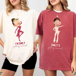 May include: Two white t-shirts with a red print. One shirt says "I'm Emily getting married" and features a cartoon image of a woman wearing sunglasses. The other shirt says "Emily's getting married" and features a cartoon image of a woman wearing sunglasses.