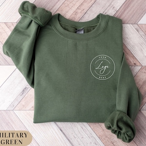 May include: A military green sweatshirt with a white circle on the front that says "Your Logo Here".