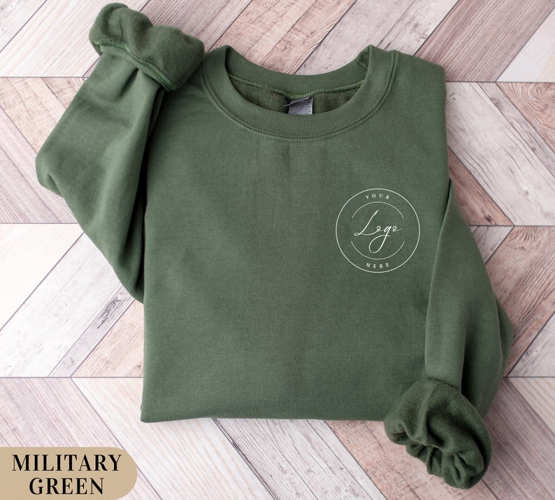May include: A military green sweatshirt with a white circle on the front that says "Your Logo Here".