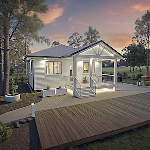 May include: A white cottage with a gray roof and a porch, set against a backdrop of trees and a sunset sky. The cottage has a wooden deck and a concrete walkway. The scene is illuminated by exterior lights.