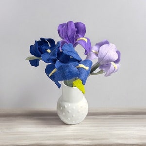 K&ouml;nnte beinhalten: Ein Strau&szlig; aus violetten, blauen und lavendelfarbenen Filz-Iris in einer wei&szlig;en Keramikvase mit Punkten.