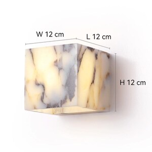 May include: A white marble cube wall sconce with a light inside. The sconce measures 12 inches in width, length, and height.