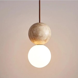 Op de afbeelding: Een moderne hanglamp met twee bollen. De bovenste bol is gemaakt van een lichtbruin, getextureerd materiaal, en de onderste bol is een witte, matte glazen bol.