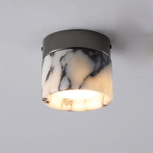 May include: A ceiling light fixture made from white marble and black metal, with a round, cylindrical shape.