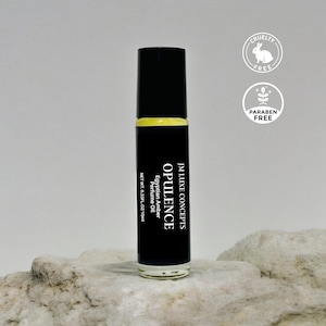 May include: A black perfume oil bottle with a yellow band, labelled "OPULENCE" and "Egyptian Amber Perfume Oil." The bottle is 10ml and features "Cruelty Free" and "Paraben Free" labels. The product is on a light grey stone surface.